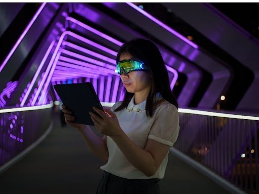 Person wearing AR smart glasses holding a tablet on a neon-lit bridge