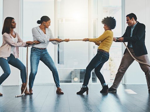 Four colleagues playing tug-of-war in an office, illustrating competing forces